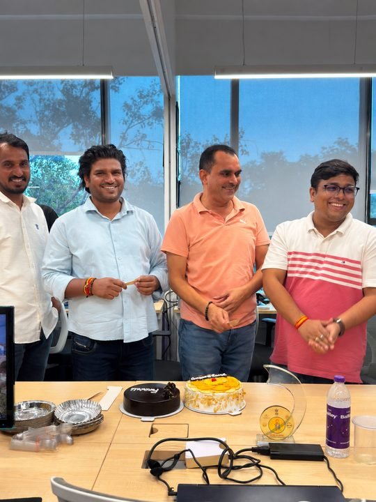 Colleagues smiling around a table with cakes during an office celebration.